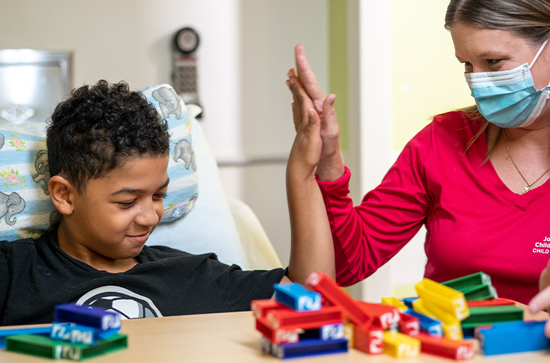 child life specialist high fiving boy in bed
